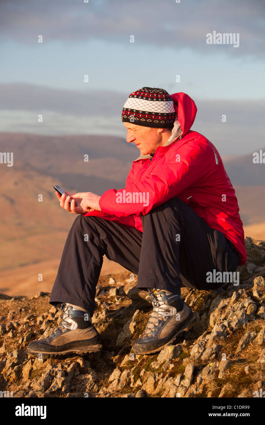 Un uomo con un iphone sulla cima di una montagna nel distretto del lago, UK. Foto Stock