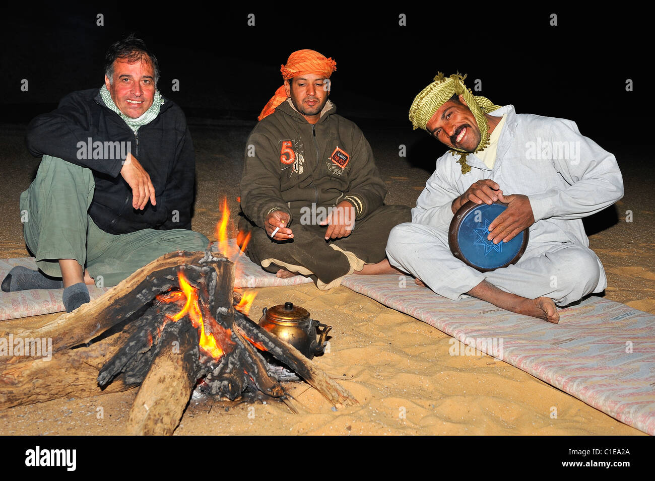 Le persone attorno a un fuoco ascoltando un musicista egiziano giocando tam timbro durante un soggiorno di una notte nel deserto bianco, Egitto Foto Stock