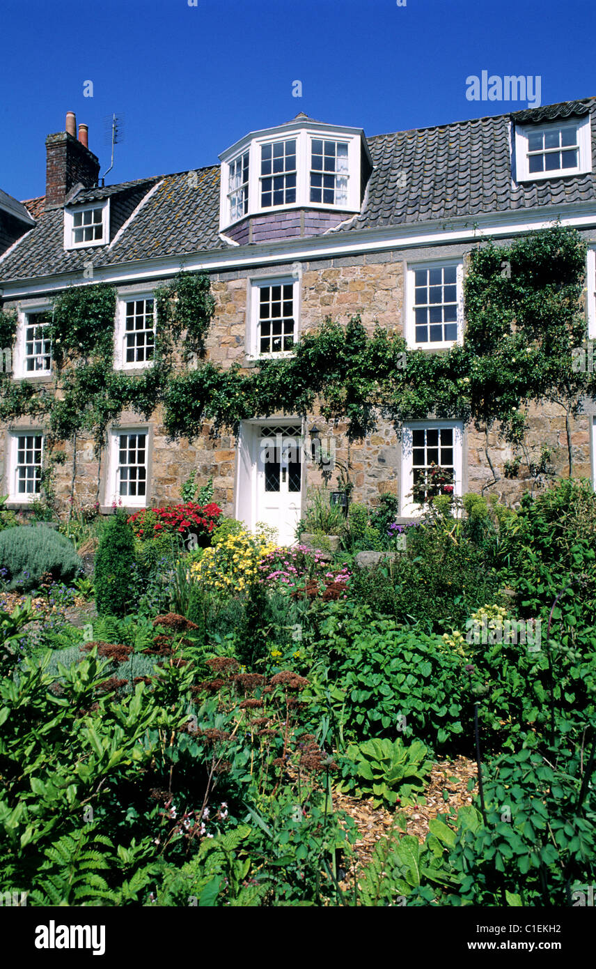 Regno Unito, Isole del Canale e Isola di Guernsey, casa circondata da fiori accanto a San Martin de la chiesa Bellouse Foto Stock