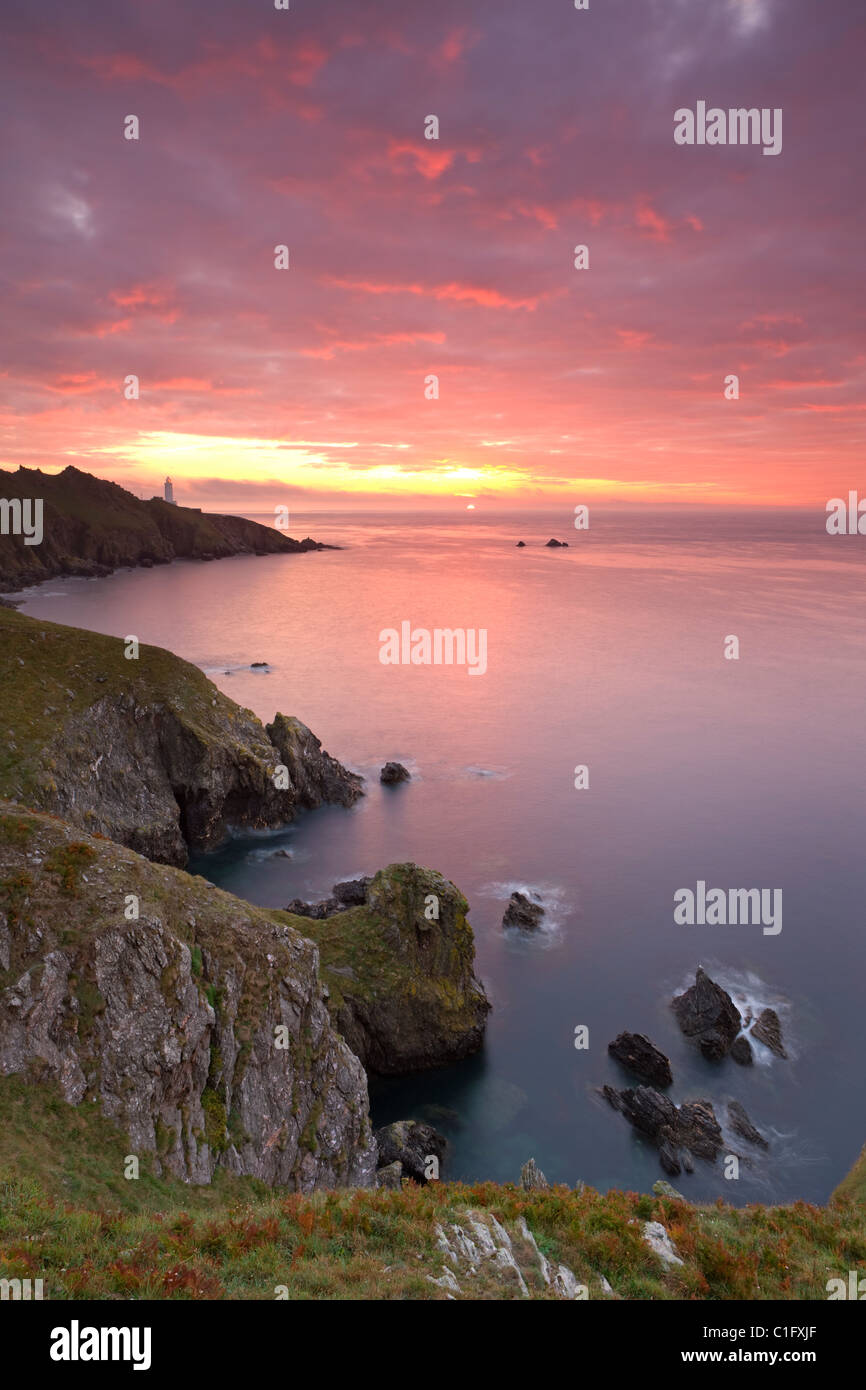 Sunrise glorioso al largo delle coste del punto di inizio con il faro sul promontorio distante, Sud prosciutti, Devon, Inghilterra. Foto Stock