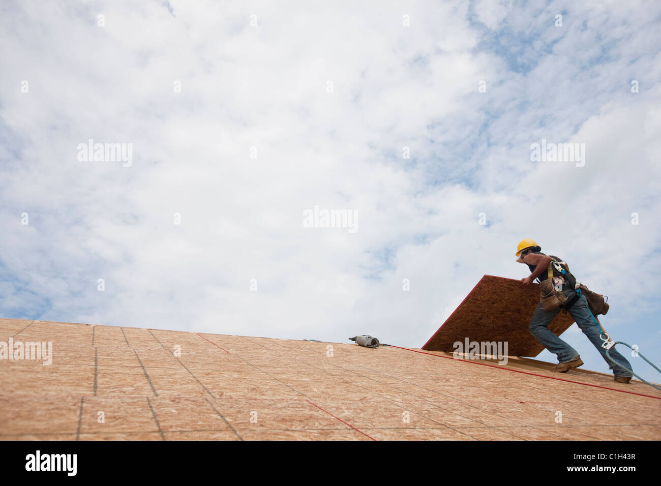 Basso angolo di visione di un falegname di sollevamento di un pannello del tetto sul tetto di una casa in costruzione Foto Stock