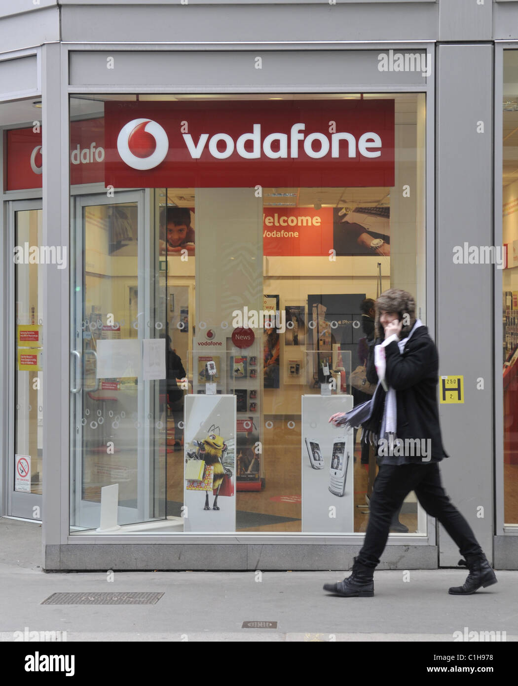 Una vista generale di un membro del pubblico a parlare su un telefono mobile a piedi passato un negozio Vodafone in Fenchurch Street a Londra Foto Stock