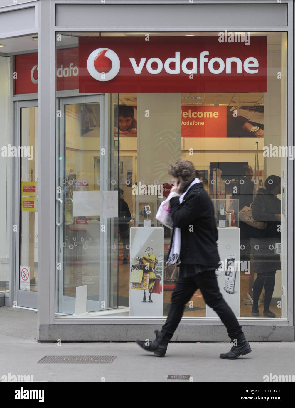 Una vista generale di un membro del pubblico a parlare su un telefono mobile a piedi passato un negozio Vodafone in Fenchurch Street a Londra Foto Stock
