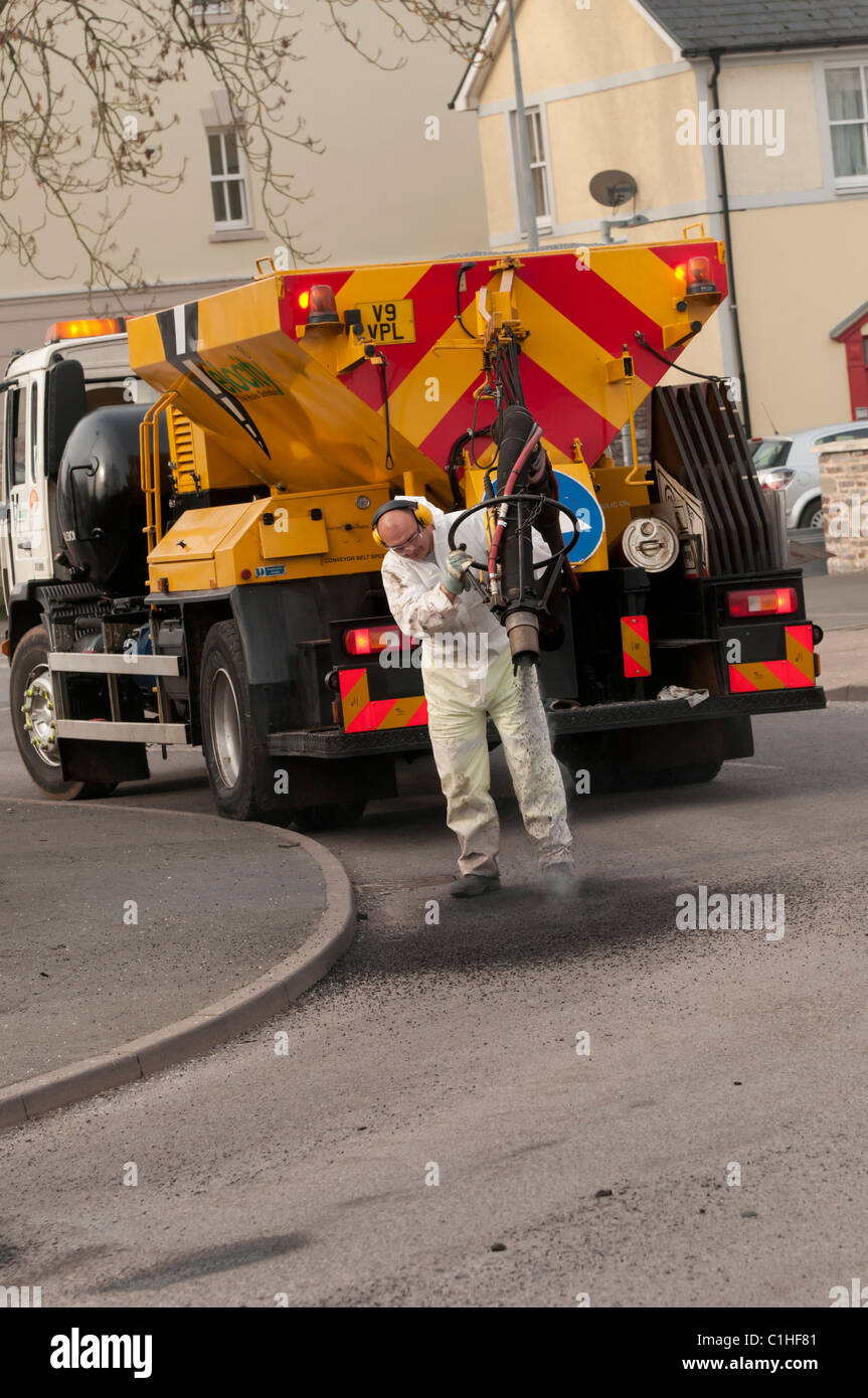 Un lavoratore di velocità di riparazione di buche in una strada con un a spruzzo ad alta pressione sistema blaster, REGNO UNITO Foto Stock