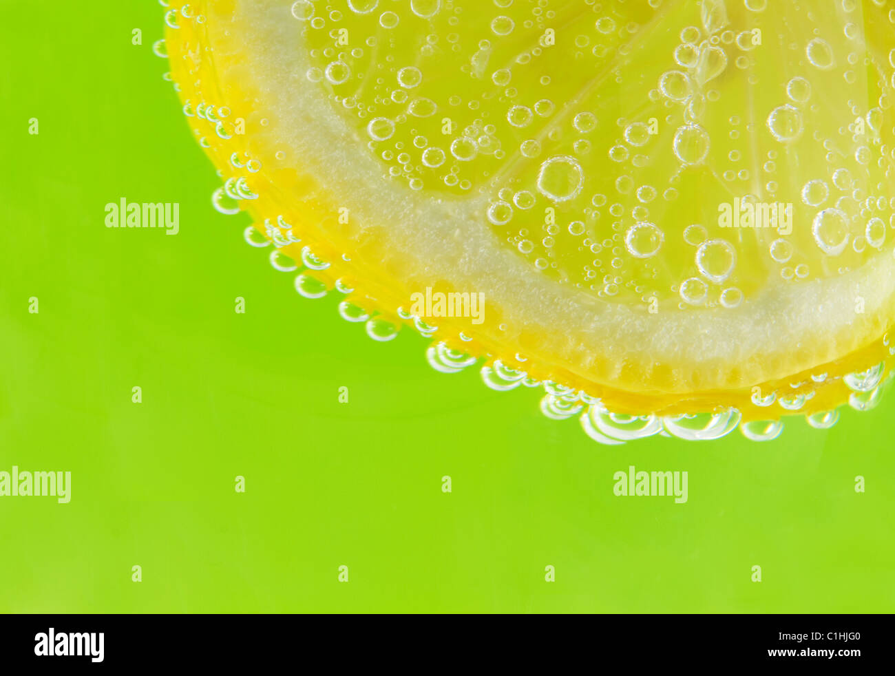Una fetta di limone è accentato con seltzer bolle contro un fresco e verde primavera sfondo. Foto Stock Una fetta di limone è accentato con seltzer bolle contro un fresco e verde primavera sfondo. Foto Stock