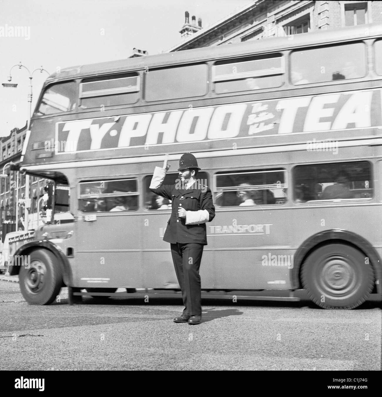 1950s, un autobus routemaster a due piani, che pubblicizza Ty-Phoo Tea, va dietro un poliziotto del traffico di segnalazione, Londra, Inghilterra, Regno Unito. Foto Stock