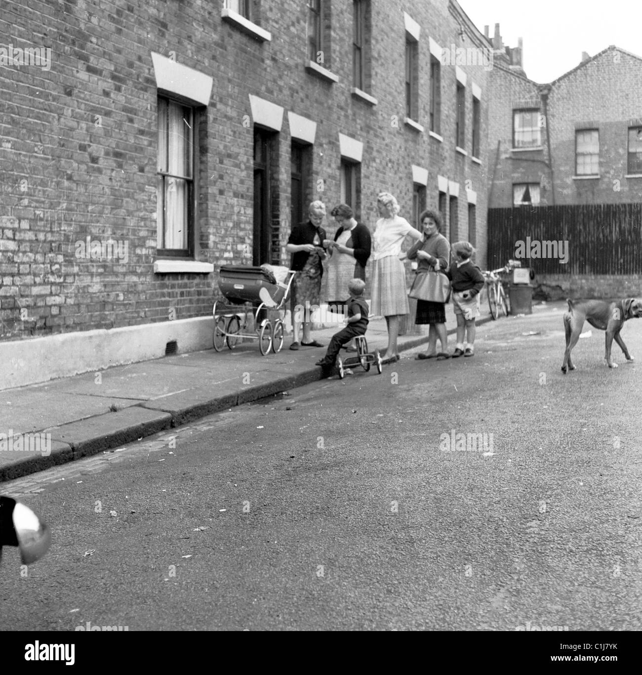 Anni Cinquanta a Londra, Inghilterra, storico, Vittoriano case a schiera, piccolo gruppo di madri al di fuori in strada con i loro figli, pram e triciclo. Foto Stock