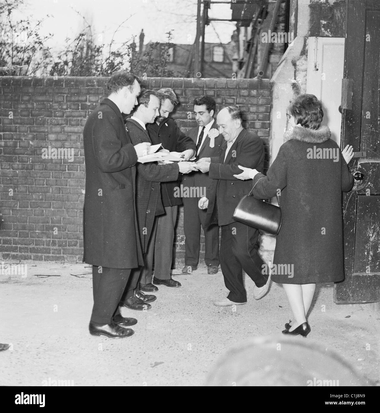 Anni '1960, storico, un uomo esce dalla sala delle votazioni a nord di Londra, per essere accolto dai rappresentanti dei diversi partiti politici britannici. Foto Stock