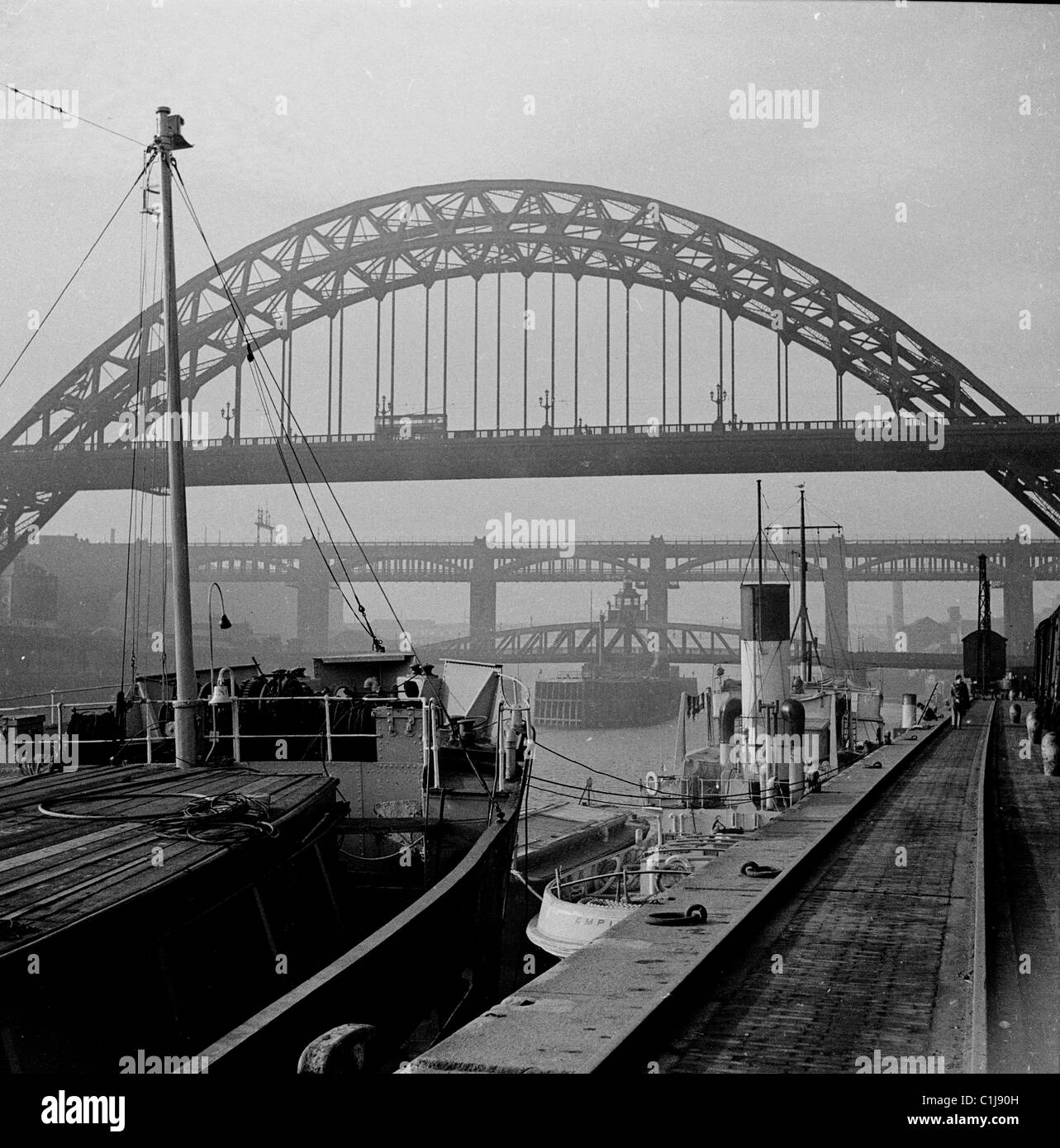 anni '1950 Barche ormeggiate nei moli mentre la nebbia copre i ponti che attraversano il fiume Tyne a Newcastleupon Tyne, Inghilterra. Il Tyne Bridge è il più vicino. Foto Stock