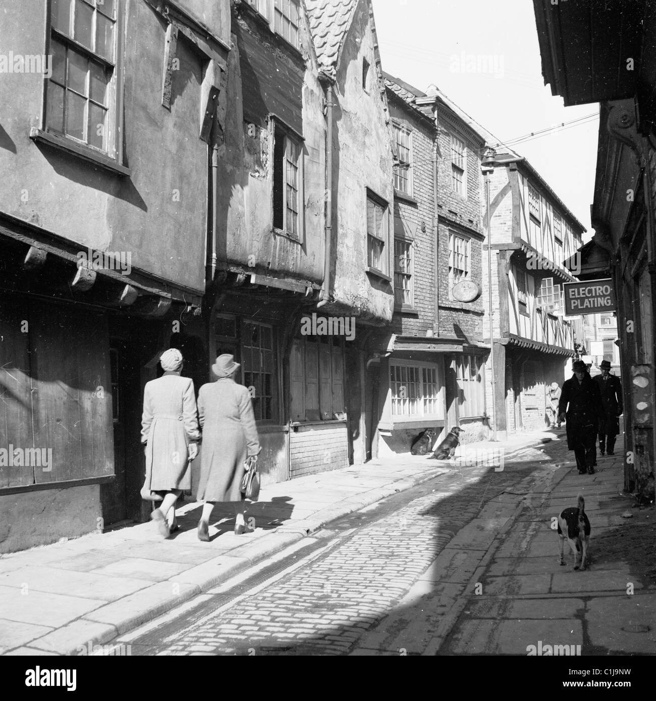 1950, un quadro storico di J Allan Cash di due signore che camminano lungo uno stretto e soleggiato vicolo acciottolato medievale in una parte vecchia di Londra, Inghilterra, Regno Unito. Foto Stock