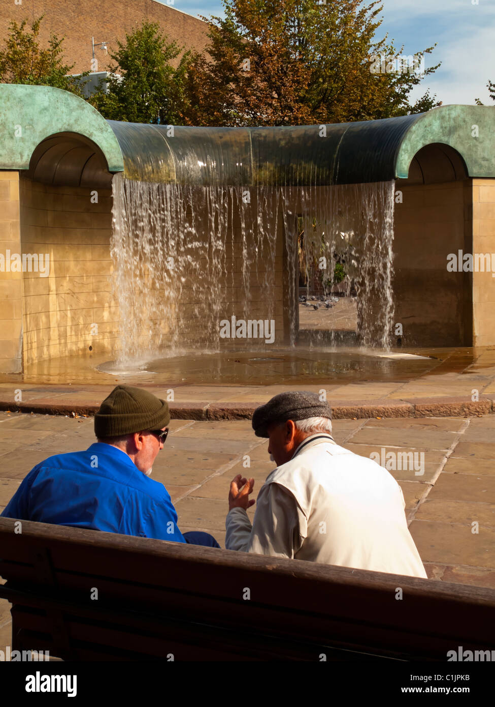 Due uomini su una panchina a parlare davanti alla fontana nella piazza del mercato in Derby city centre Derbyshire England Regno Unito Foto Stock