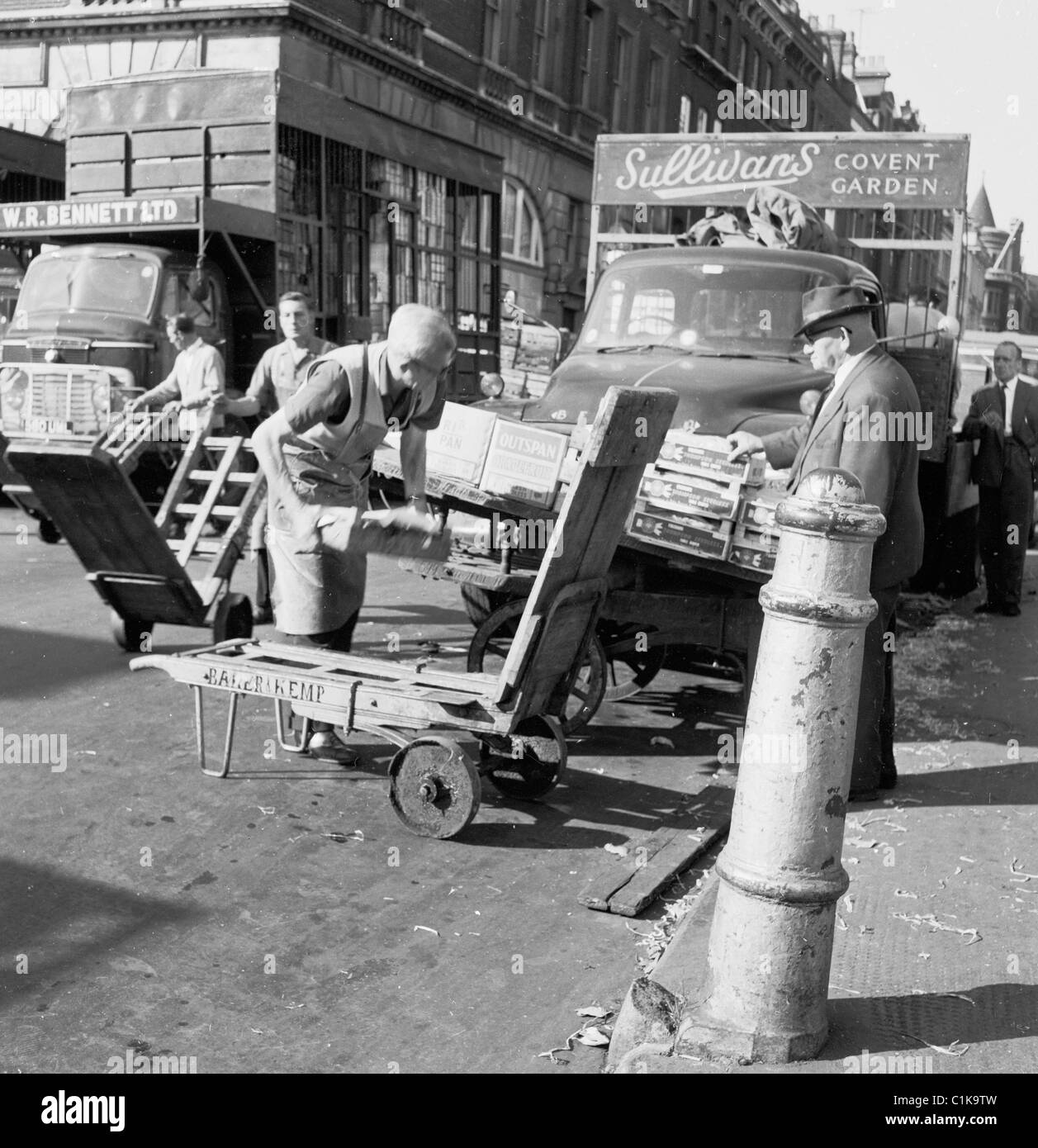 1950s. Fattorino all'al mercato di frutta e verdura in Covent Garden, carico il suo carrello, mentre in fase di studio da parte di un uomo anziano. Foto Stock