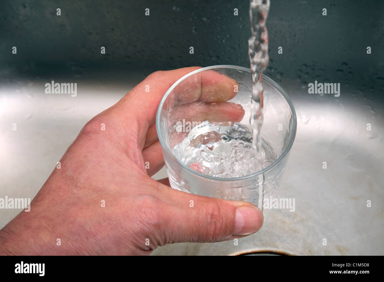 L'uomo riempire un bicchiere con acqua da un rubinetto da cucina. Foto Stock