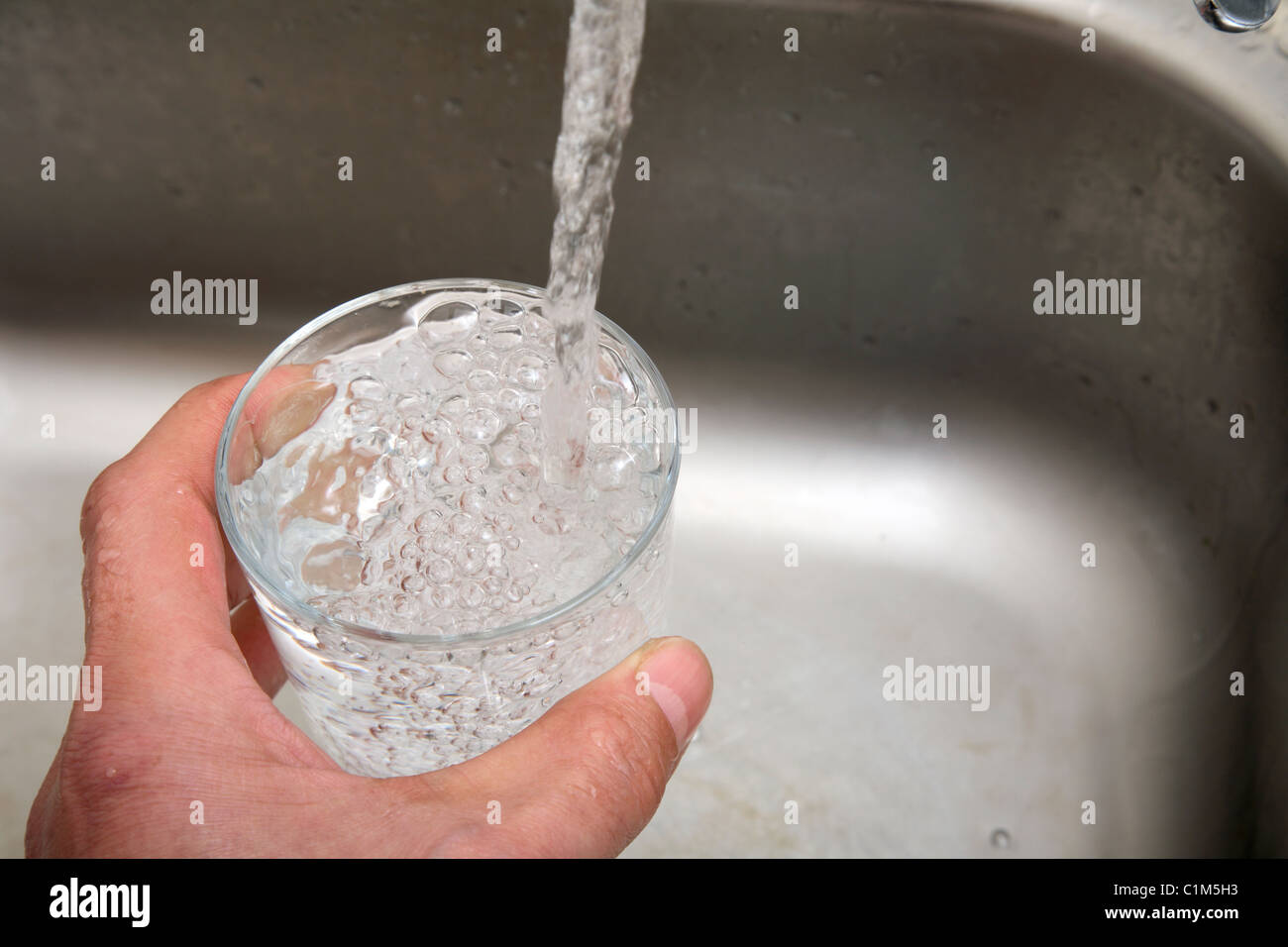 L'uomo riempire un bicchiere con acqua da un rubinetto da cucina. Foto Stock