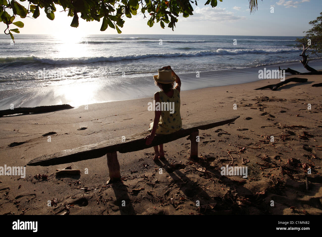 Una donna si siede su una panchina a guardare il tramonto sulla Playa Avellanas, Nicoya peninsula, Costa Rica Foto Stock