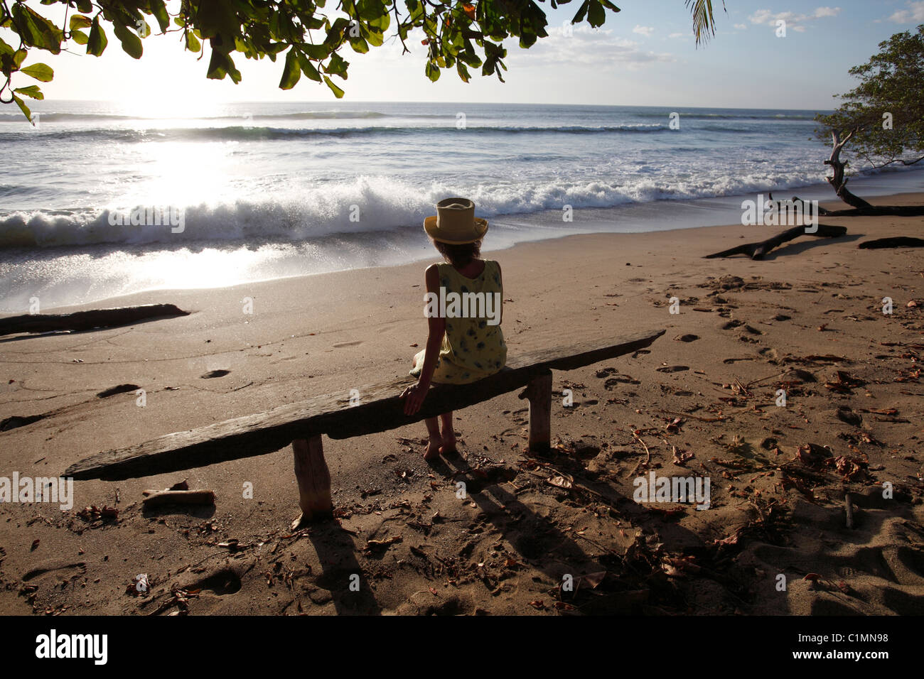 Una donna si siede su una panchina a guardare il tramonto sulla Playa Avellanas, Nicoya peninsula, Costa Rica Foto Stock