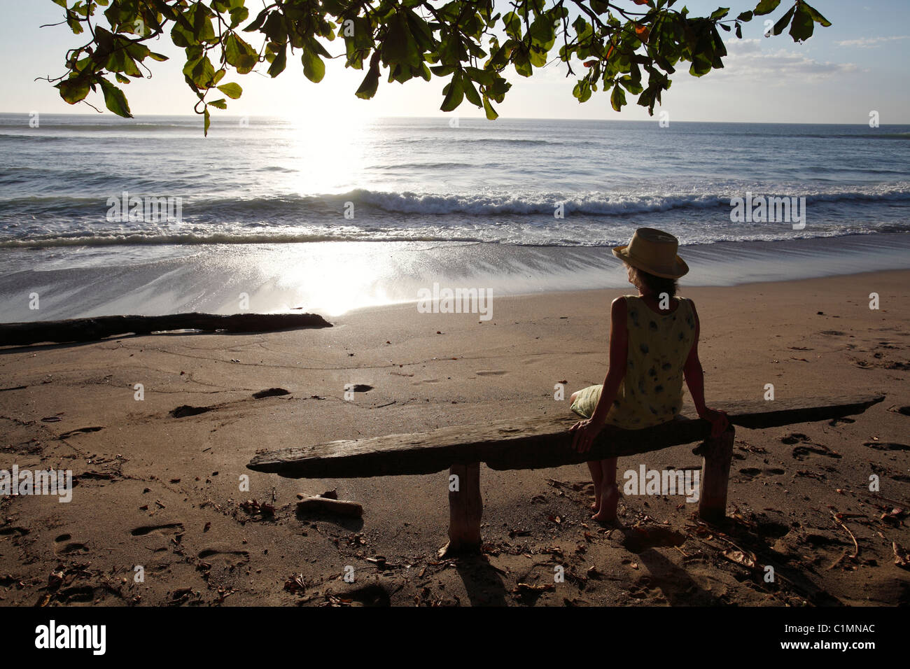 Una donna si siede su una panchina a guardare il tramonto sulla Playa Avellanas, Nicoya peninsula, Costa Rica Foto Stock