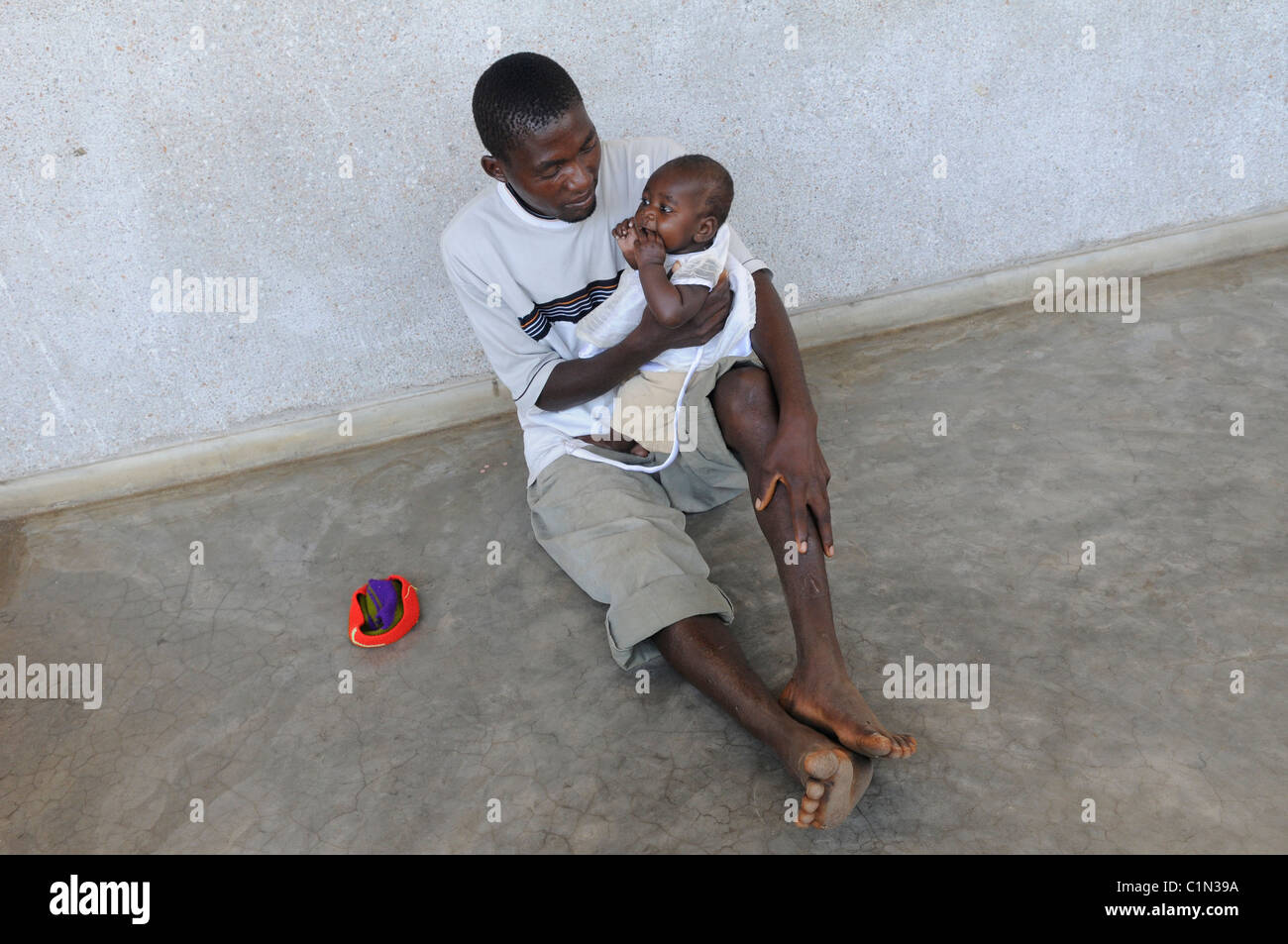 Un uomo si siede sul pavimento e mantiene il suo figlio in Africa Malawi Foto Stock