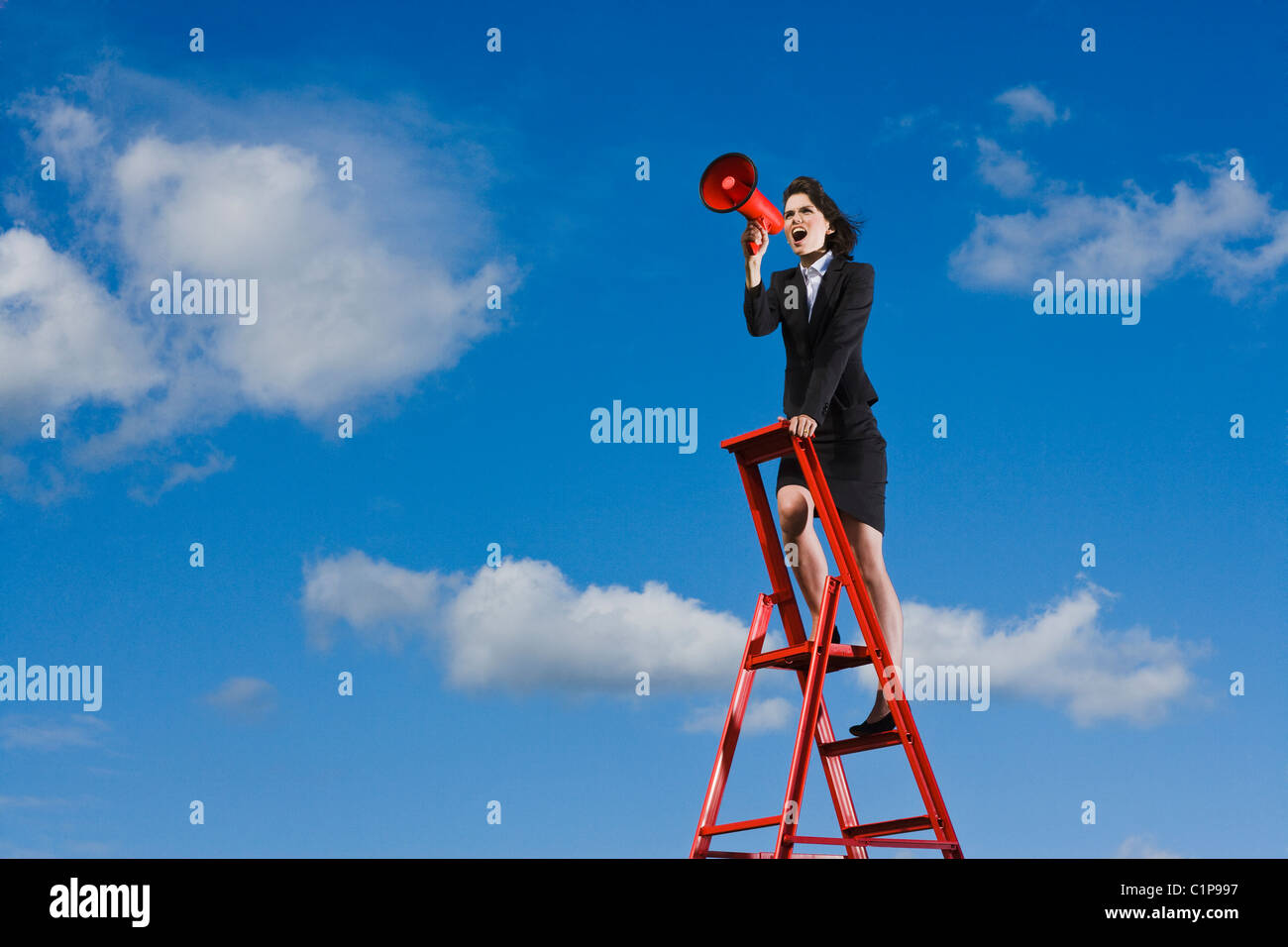 Imprenditrice permanente sulla parte superiore della scaletta rosso contro il cielo blu e urlando attraverso il red megafono Foto Stock