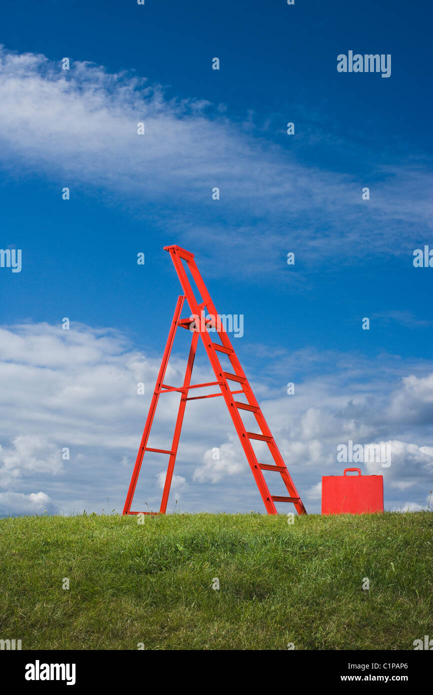 La scala di colore rosso e rosso valigetta in campo in erba contro il cielo blu Foto Stock