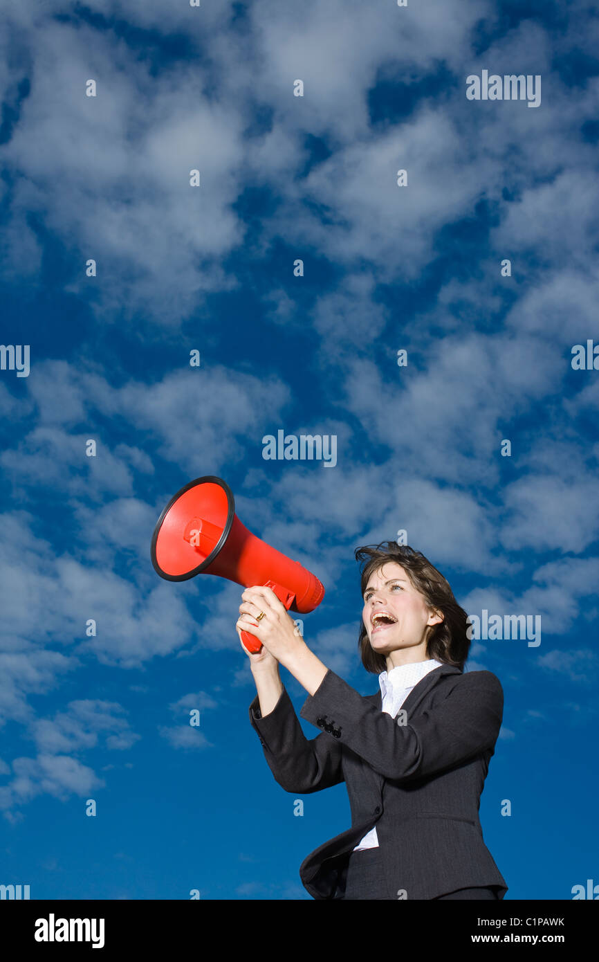 Imprenditrice contro il cielo blu e urlando attraverso il red megafono Foto Stock