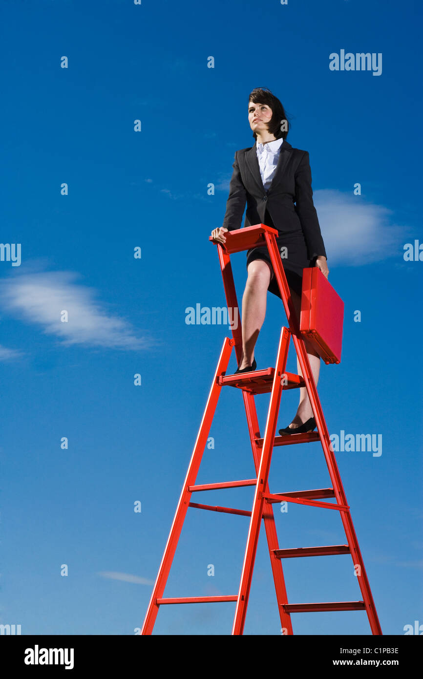 Imprenditrice con valigetta rosso permanente sulla parte superiore della scaletta rosso contro il cielo blu Foto Stock
