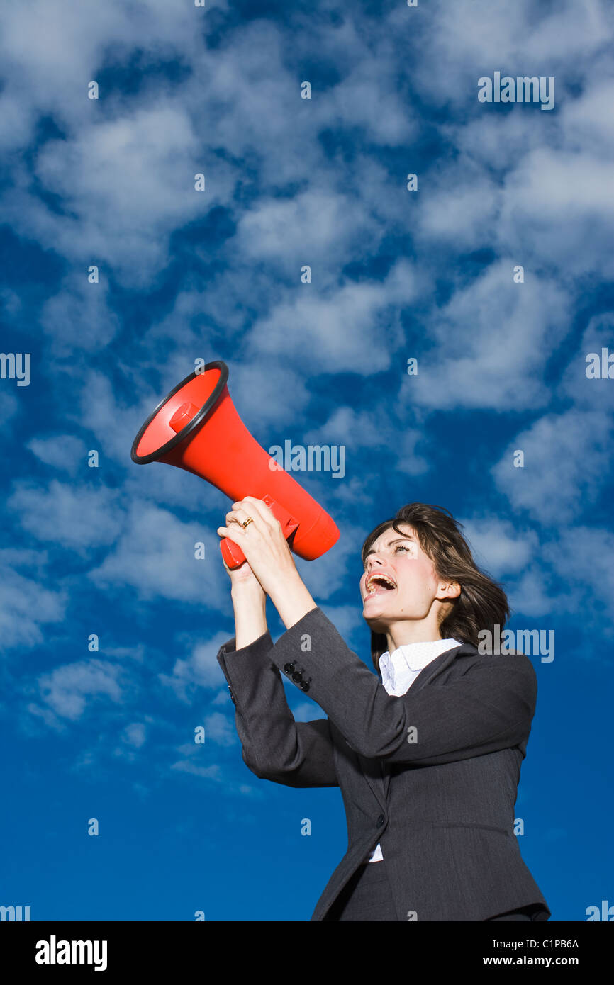 Imprenditrice contro il cielo blu e urlando attraverso il red megafono Foto Stock