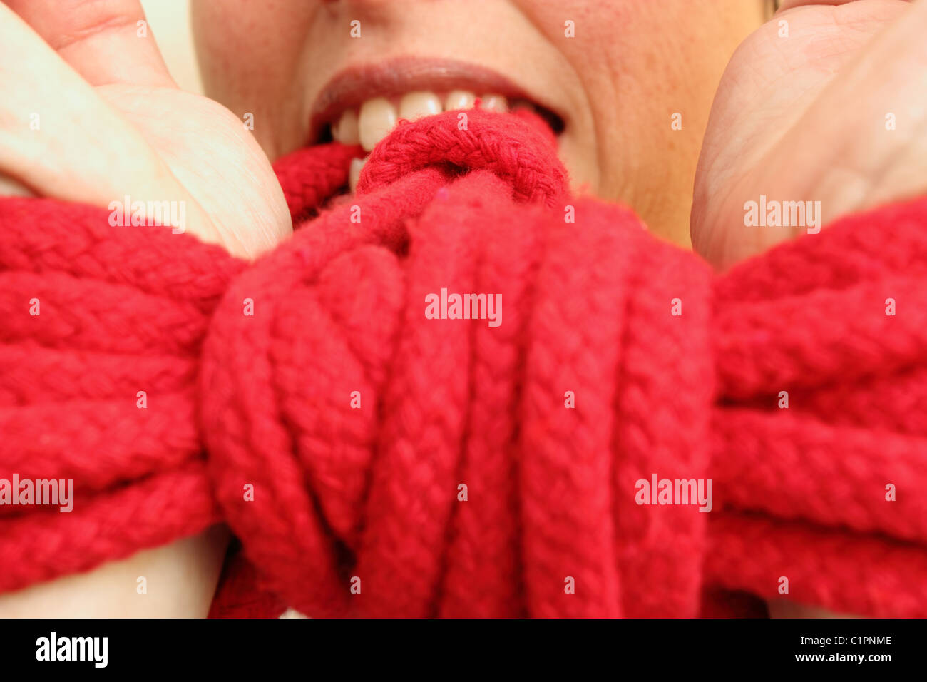 Donna che utilizza i suoi denti a tirare i suoi polsi legati con corda rossa Foto Stock