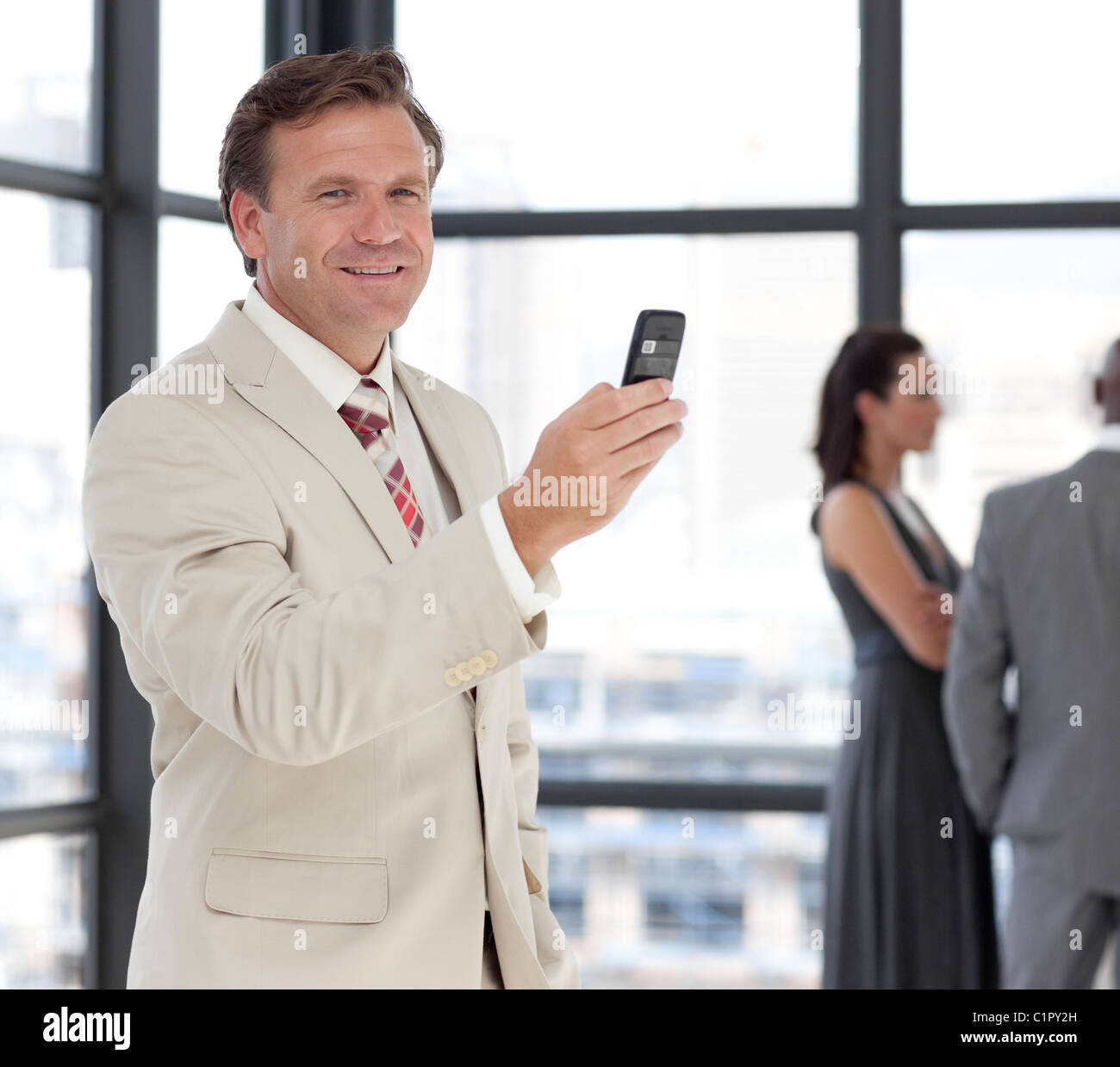 Happy businessman tenendo un telefono al posto di lavoro con i colleghi Foto Stock