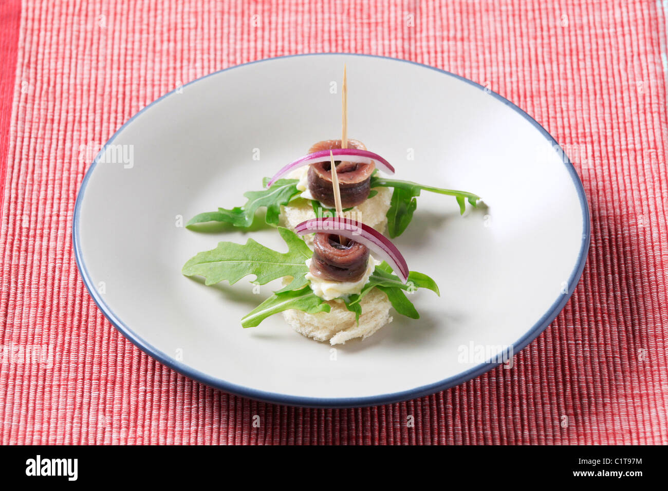 Crostini di acciuga guarnite con foglie di rucola e cipolla Foto Stock