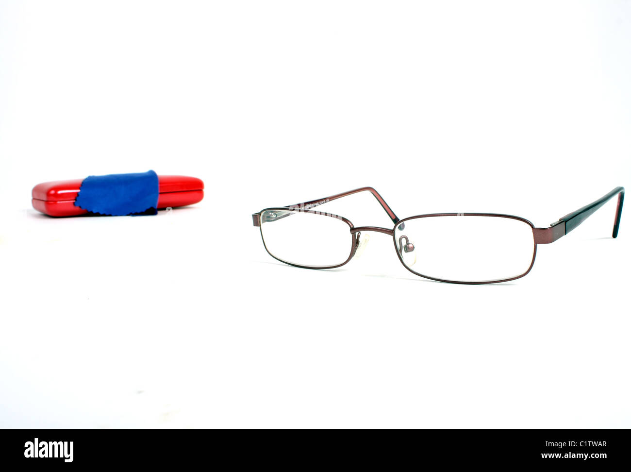 Una coppia di borgogna gli occhiali da lettura su un bianco di fondo tagliato con un rosso custodia per occhiali e panno blu per pulizia. Foto Stock