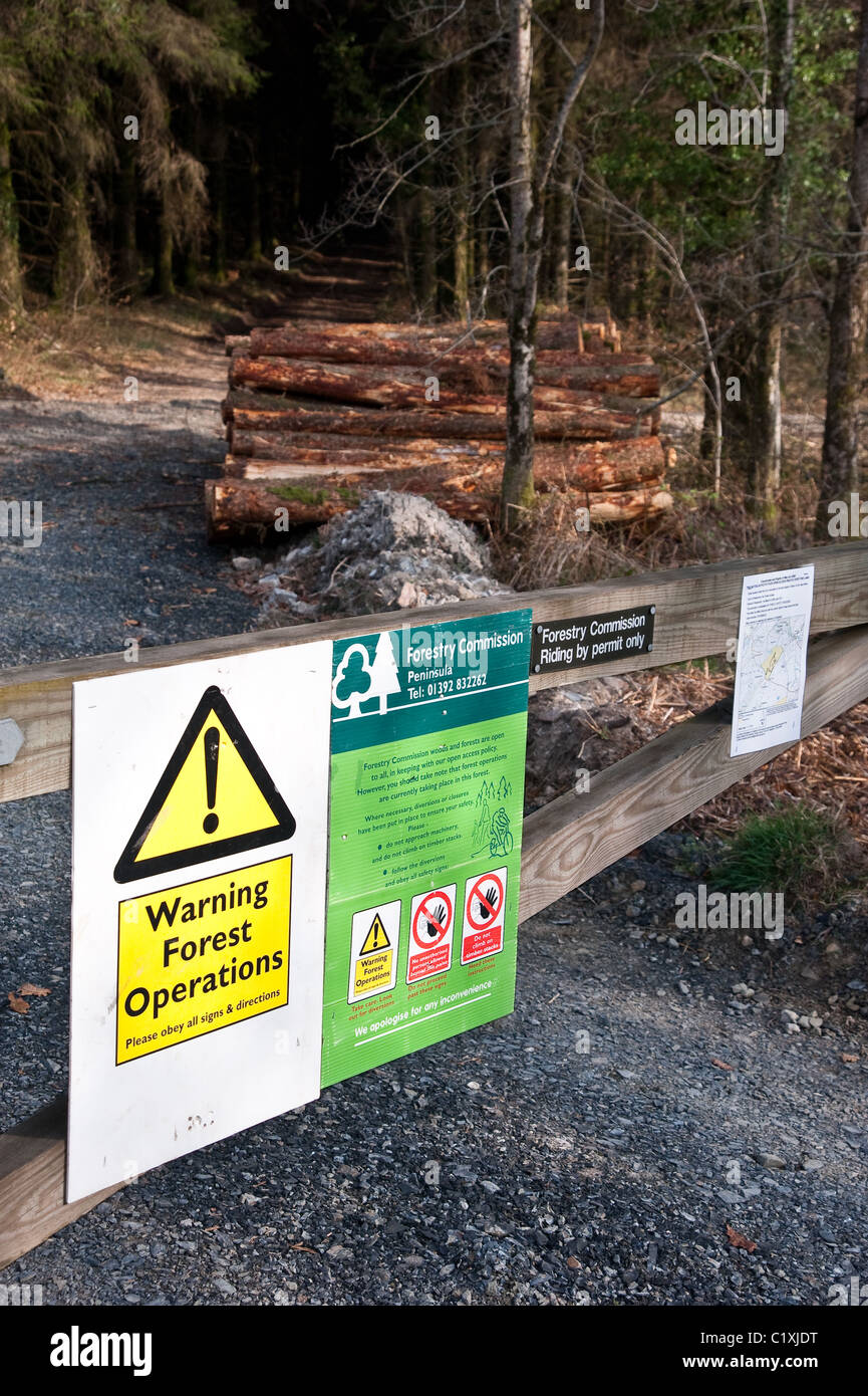 Avvisi su un cancello in una commissione forestale avviso di bosco di abbattimento nella zona con una pila di taglio fresco logs Foto Stock