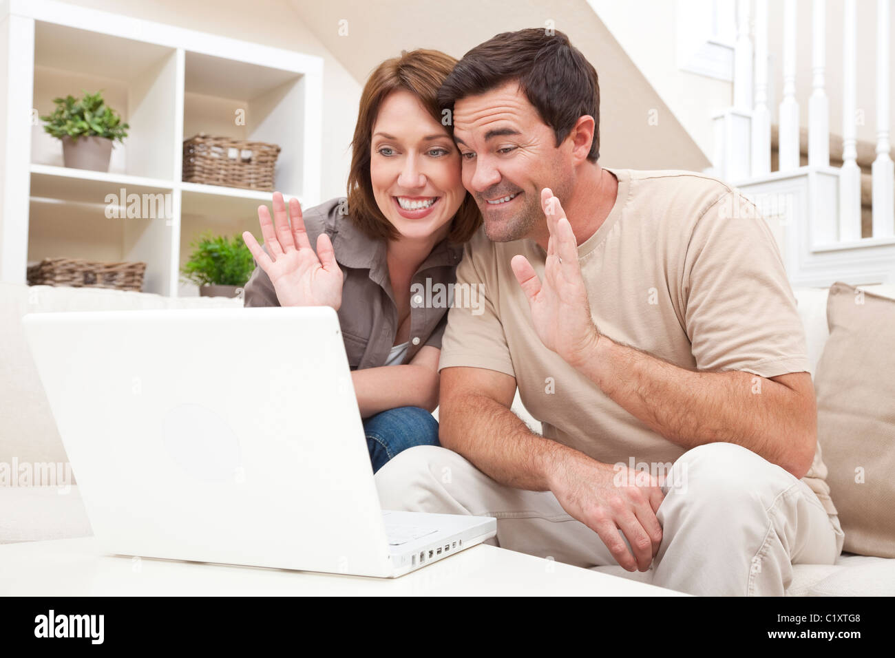 Felice l'uomo e la donna giovane, seduti insieme a casa su un divano con un computer portatile per effettuare una via internet con il servizio VOIP chiamata telefonica Foto Stock
