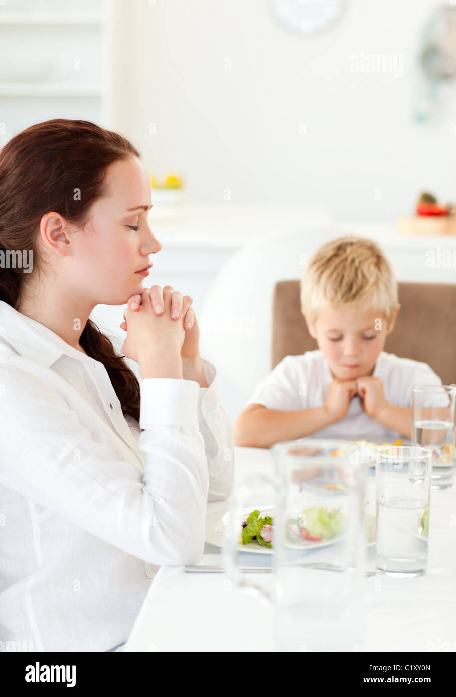 Concentrato di madre e figlio pregando durante il pranzo Foto Stock