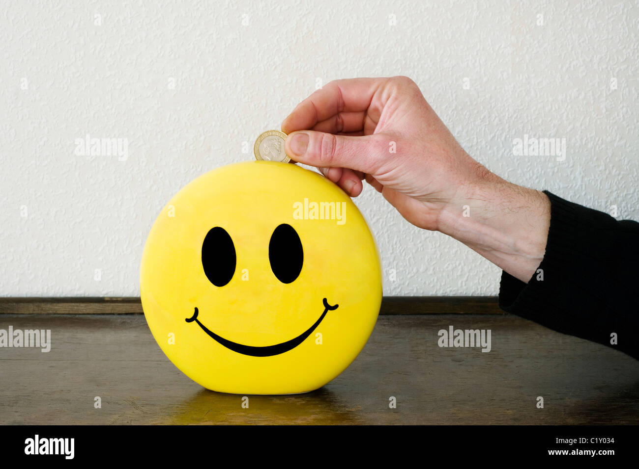 Uomo di mettere il denaro in un risparmio smiley box Foto Stock