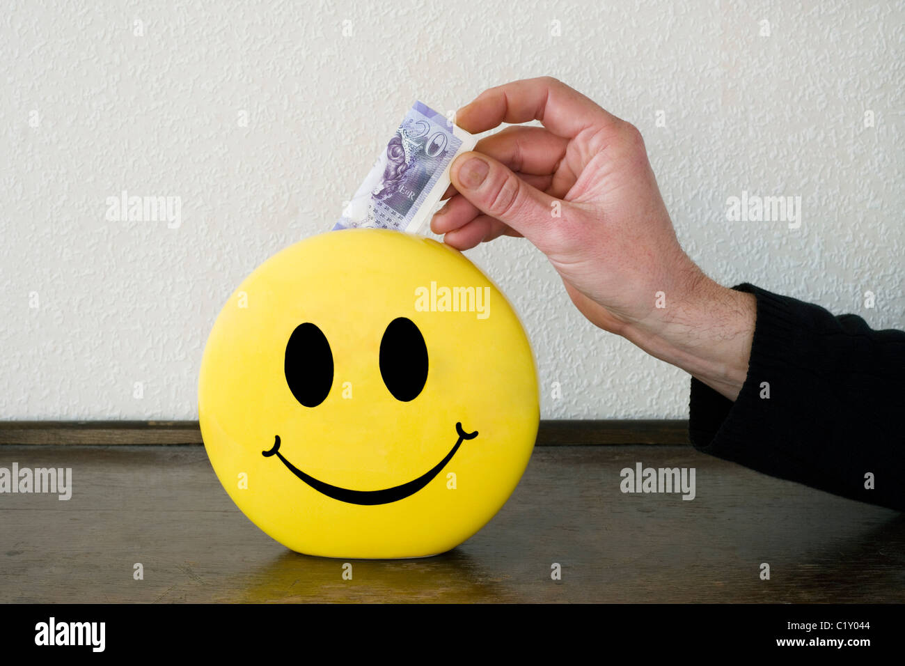 Uomo di mettere il denaro in un risparmio smiley box Foto Stock