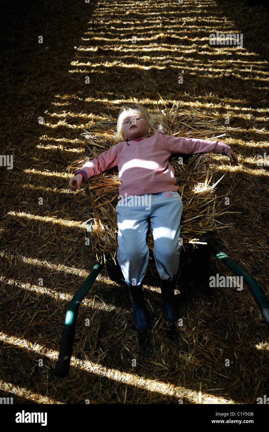 Stock Foto di una bambina di cinque anni che giace su una carriola riempita di paglia. Foto Stock