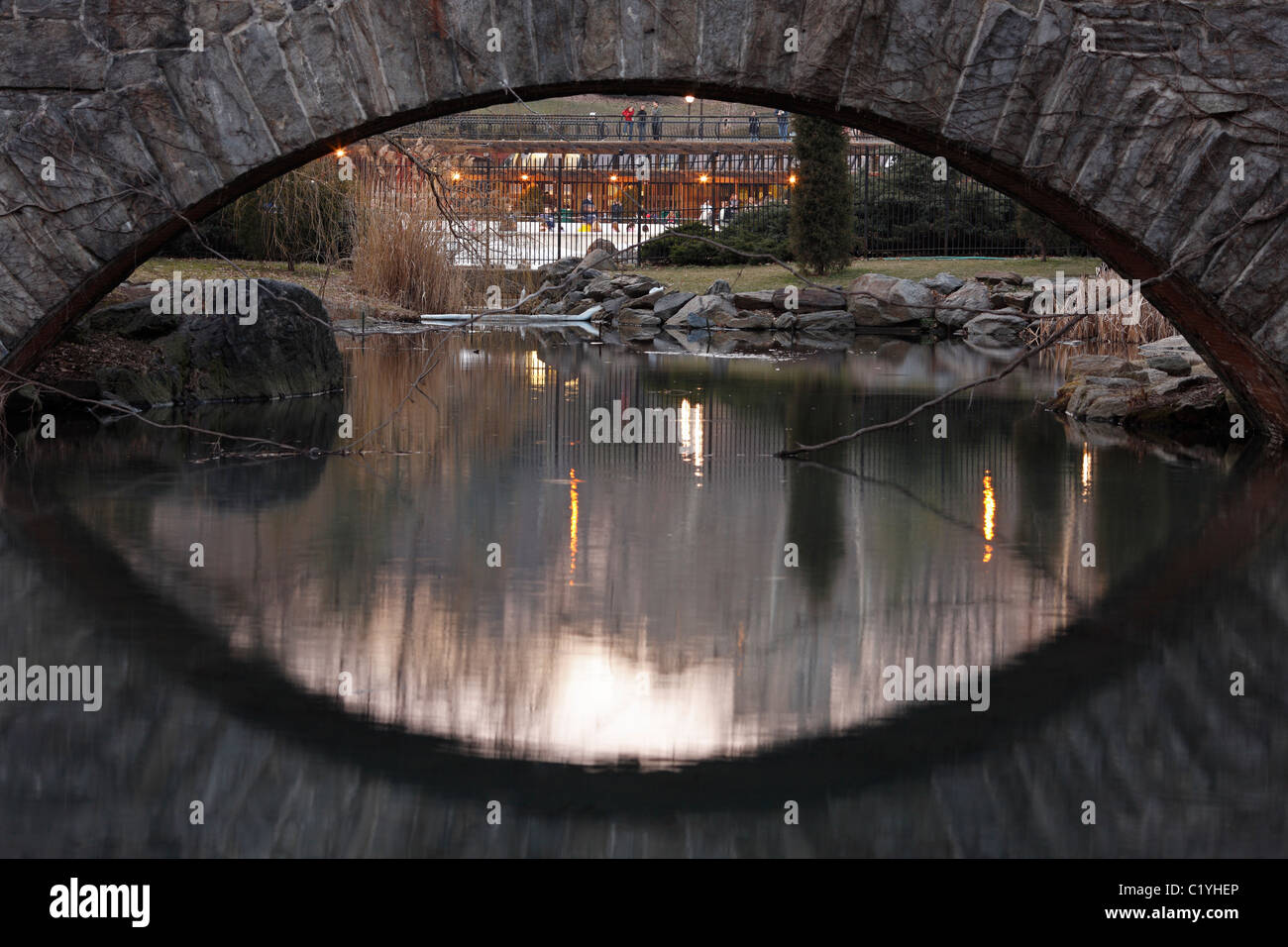 Gapstow Bridge come visto dal laghetto con riflessi nell'acqua e una vista di Wollman rink Foto Stock
