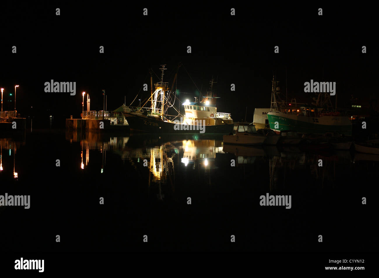 Imbarcazione da pesca illuminata di notte nel porto interno di Padstow con riflesso della barca sull'acqua stalla. Pescherecci a strascico che si preparano a navigare in alta marea. Foto Stock