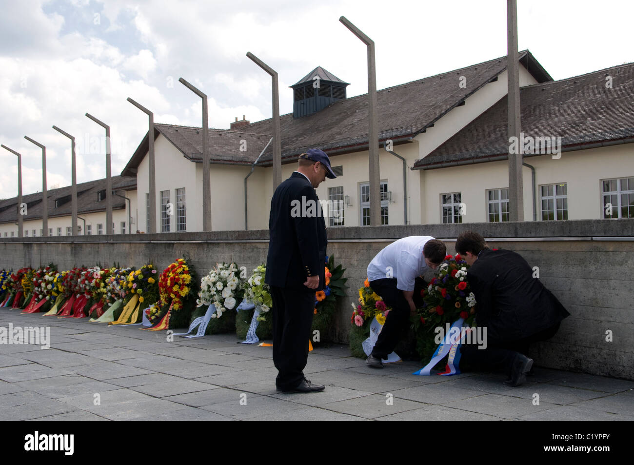I visitatori che stabilisce ghirlanda di fiori durante il giorno memoriale nel campo di concentramento di Dachau, Baviera, Germania Foto Stock