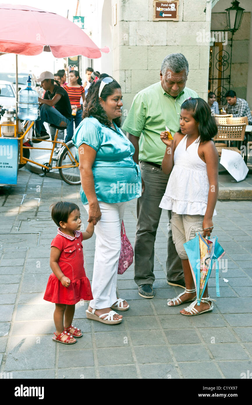 Mexican tween girl legge la sua fortuna in Oaxaca Zocalo mentre i membri della famiglia madre padre & carino sorellina guardare sul Messico Foto Stock