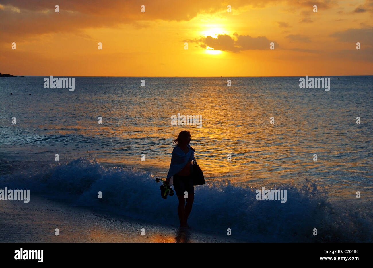 Giovane donna a piedi linea surf Oceano Indiano surf al tramonto, Seicelle Foto Stock