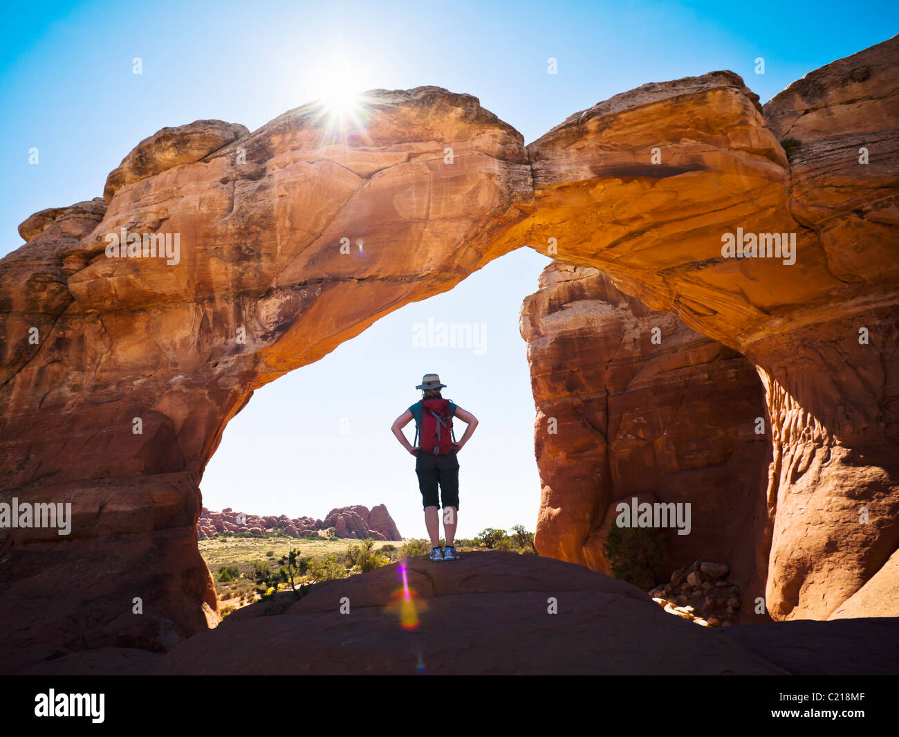 Una donna escursionista sorge sotto arco spezzato nel Parco Nazionale di Arches, Utah, Stati Uniti d'America. Foto Stock