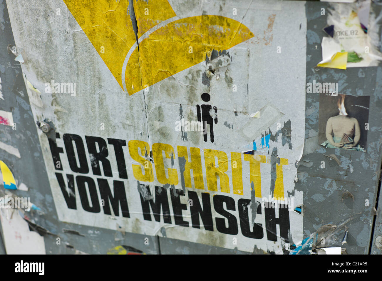 Locandina su 'FORTSCHRITT VOM MENSCH' mostra una piccola persona che si trova sotto un abstract giallo piede, Gärternplatzviertel, Monaco di Baviera Foto Stock