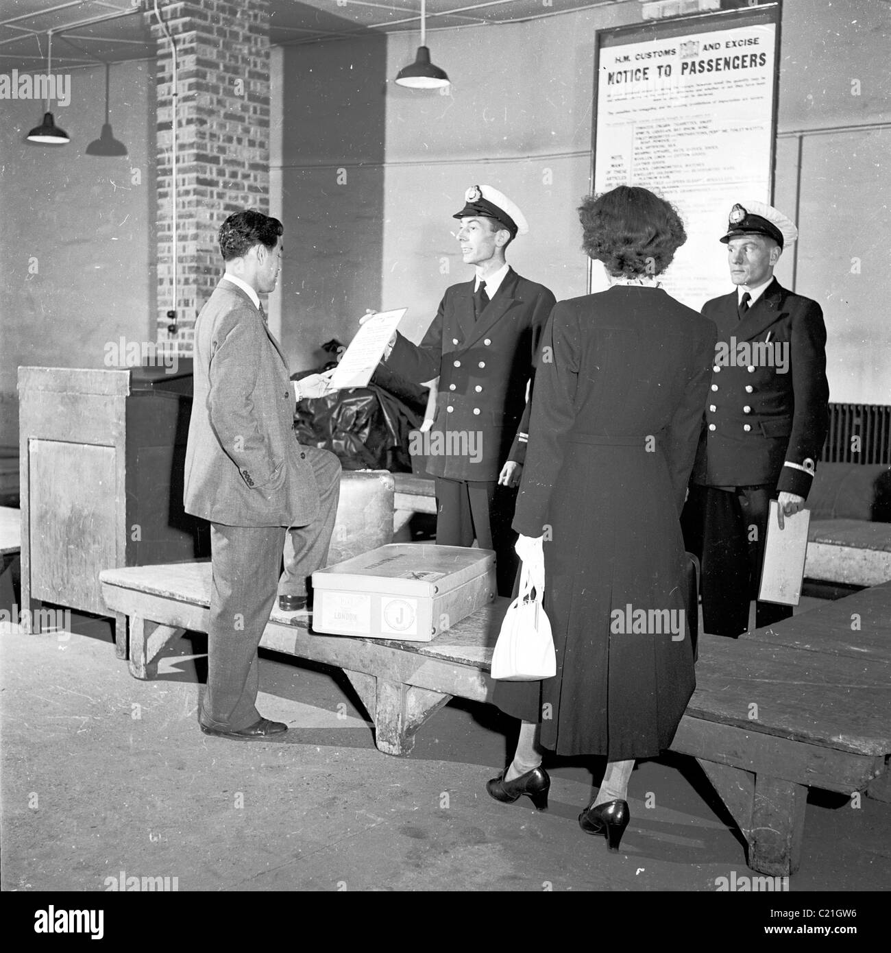 1950, storico, un visitatore d'oltremare appena arrivato in Gran Bretagna che ha mostrato un avviso da parte di ufficiali doganali uniformi ad un controllo del bagaglio, Inghilterra. Foto Stock