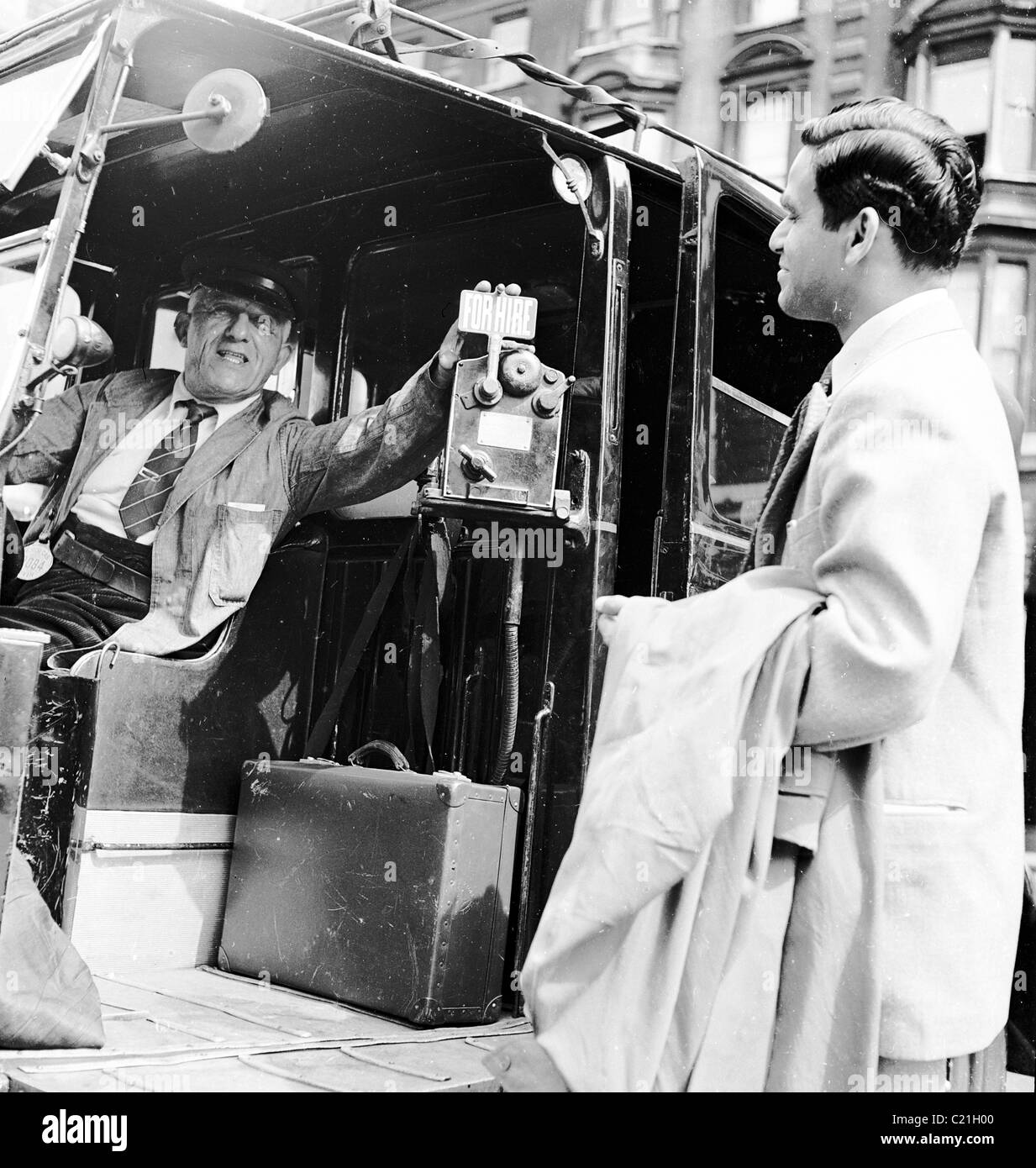 1950, un immigrato maschio appena arrivato in Gran Bretagna, in una tuta &con cappotto e valigetta, ottenendo un taxi di Londra in questa foto storica di J Allan Cash. Foto Stock