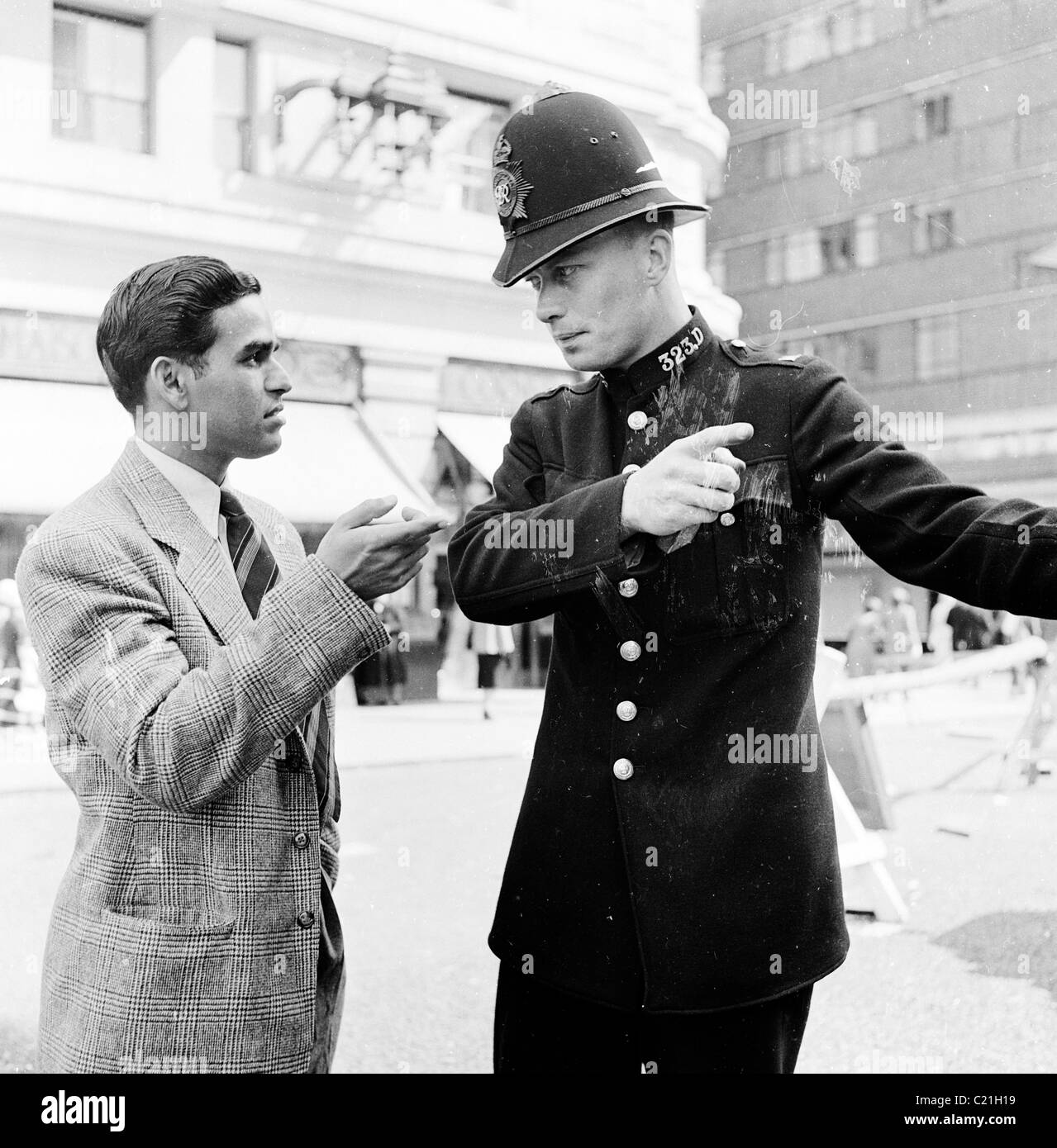 1950s, storico, Londra e un immigrato appena arrivato nel Regno Unito riceve indicazioni da un poliziotto britannico in uniforme e casco dell'epoca. Foto Stock