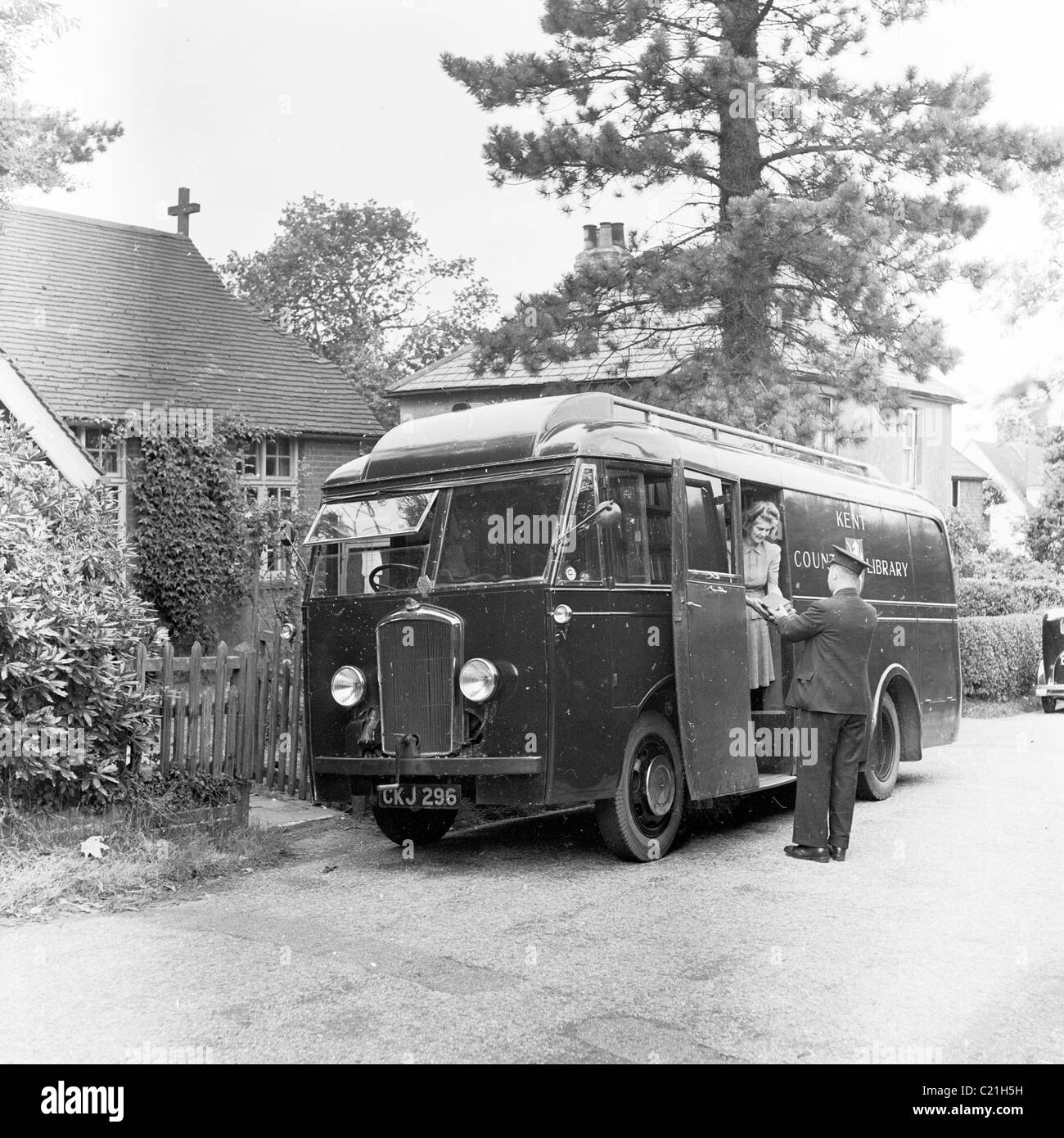 1950s, una biblioteca mobile parcheggiata in una corsia nel Kent, Inghilterra, Regno Unito, con un autista in uniforme con cappello che aiuta una signora con libri sui gradini laterali del veicolo Foto Stock