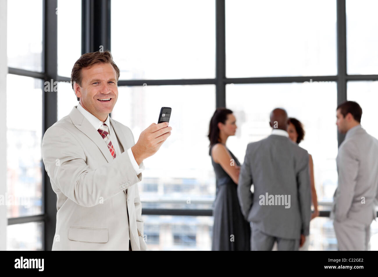 Fiducioso imprenditore tenendo un telefono al posto di lavoro con i colleghi Foto Stock