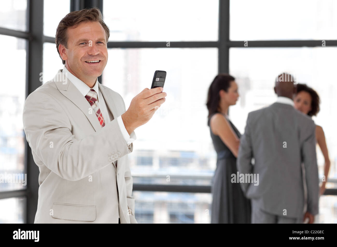 Imprenditore carismatico tenendo un telefono al posto di lavoro con i colleghi Foto Stock